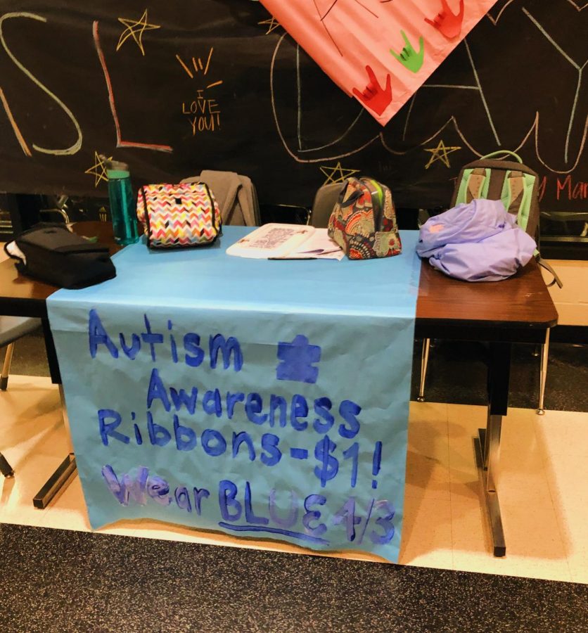 A table selling Autism Awareness ribbons is placed outside the cafeteria during lunch for students to buy.